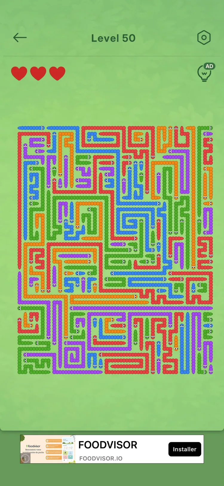 A crowded caterpillar level in Amaze Go — a green board packed edge to edge with red, orange, blue, green and purple caterpillars, each with a little face